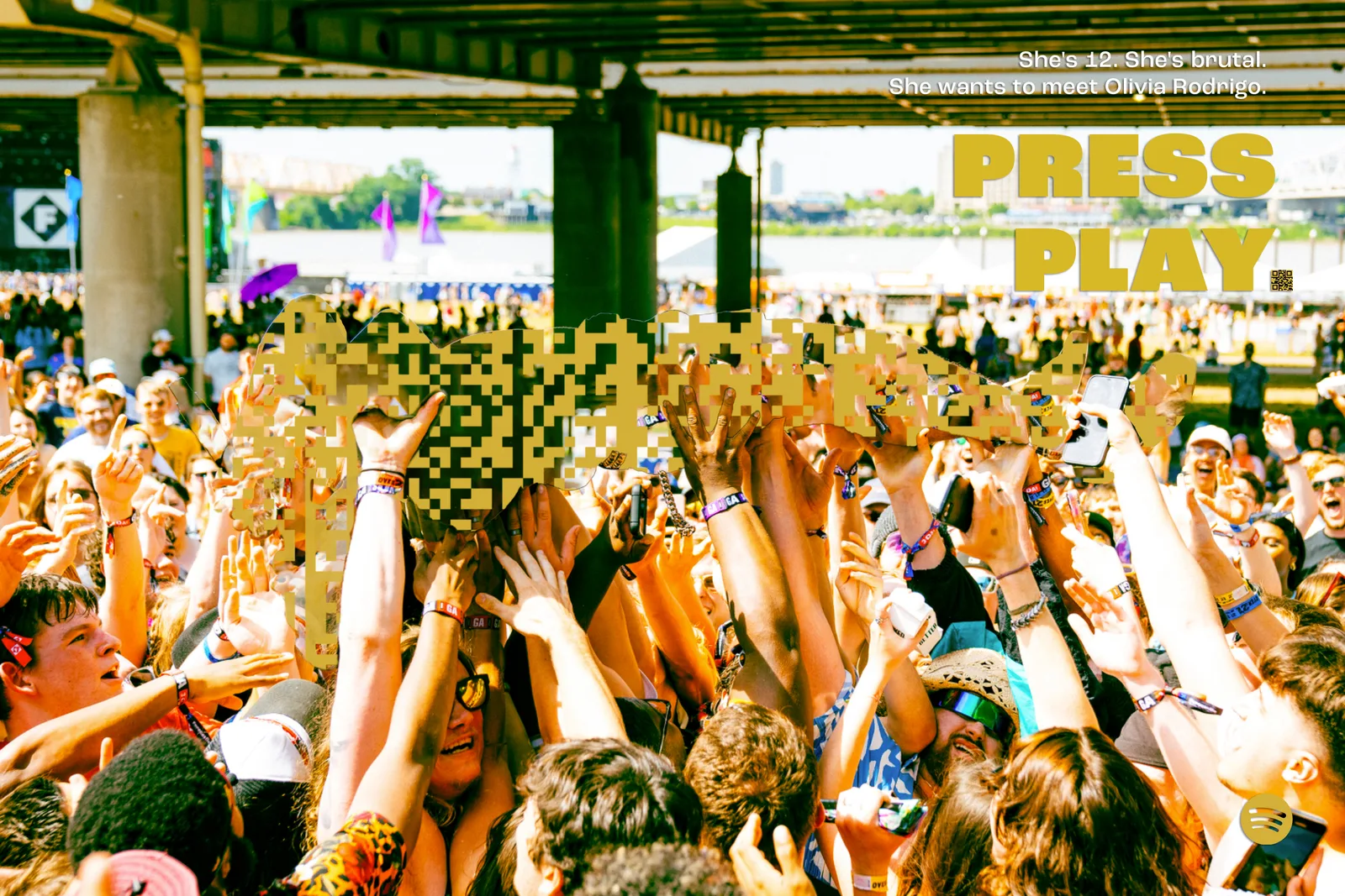 Sunlit waterfront festival under a bridge, a large gold code crowdsurfer. Headline, She's 12. She's brutal. She wants to meet Olivia Rodrigo. Press play.