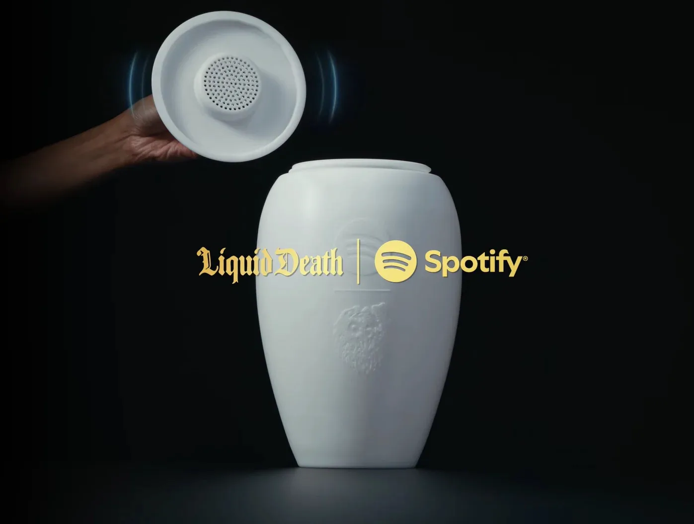 A white ceramic urn with a Liquid Death and Spotify lockup, its lid lifted to reveal a built-in speaker