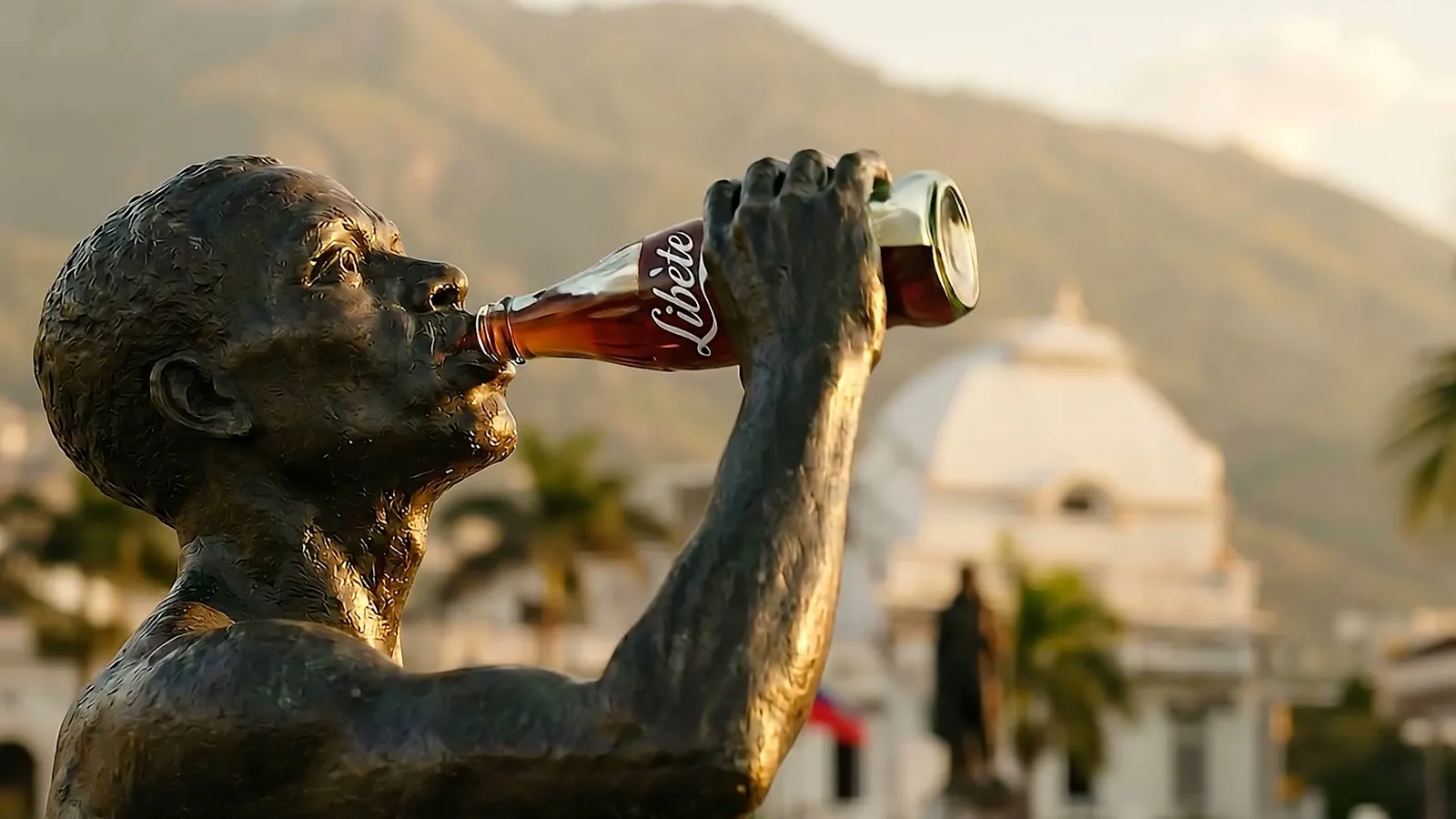 Frame from the film, the same statue tipping a Coca-Cola bottle reading Libète back to drink