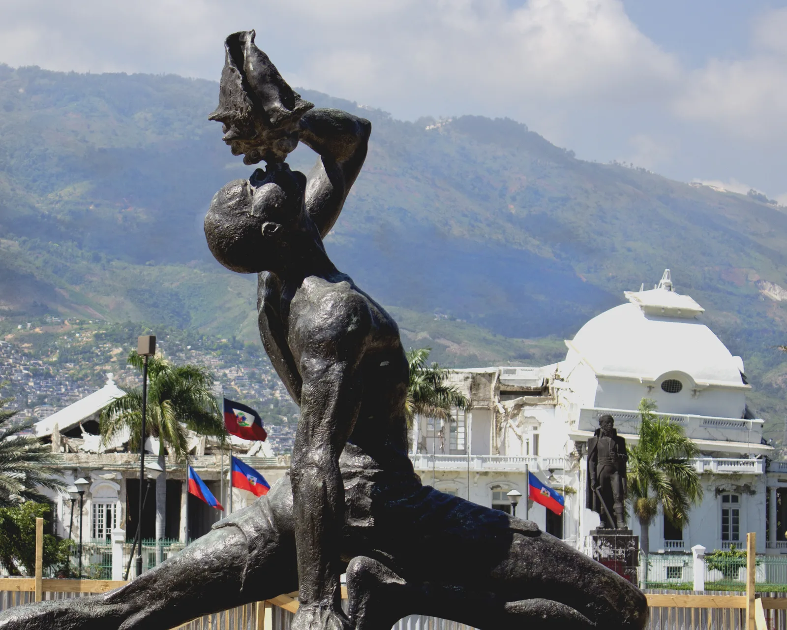 Photograph of Le Marron Inconnu in Port-au-Prince, blowing a conch, the National Palace behind