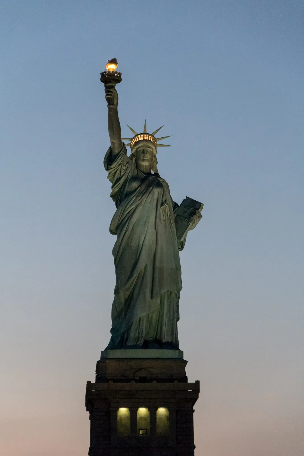 Photograph of the Statue of Liberty at dusk, torch lit